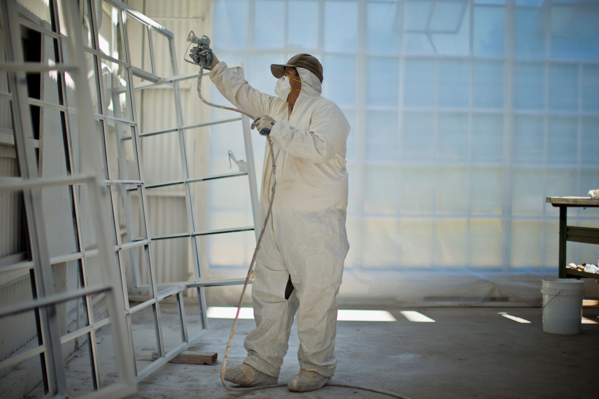 Mid adult man in protective clothing spray painting window frames inside a garage.